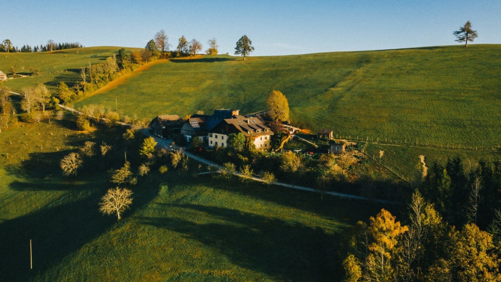 Luftaufnahme des Bauernhofs, umgeben von grünen Hügeln und Bäumen