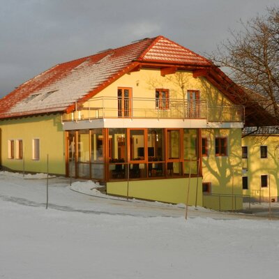 Außenansicht des Bauernhofs im Winter, mit dem verglasten Wintergarten und einem Balkon, umgeben von Schnee.