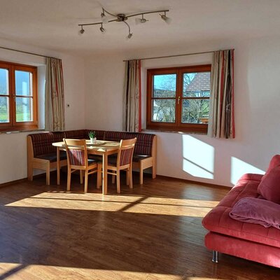 Der Wohn- und Essbereich der Ferienwohnung im Bauernhof mit Eckbank, Esstisch und einem roten Sofa.