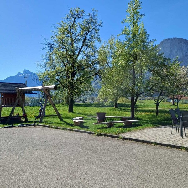 Der Kinderspielplatz mit Spielhaus und Schaukel sowie die Sitzgelegenheiten im Freien auf dem Bauernhof, mit Blick auf die umliegenden Wiesen und Berge.