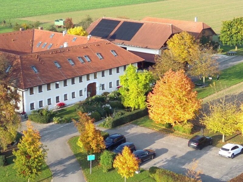 Luftaufnahme des Bauernhofs mit Hauptgebäude, Parkplatz und Kinderspielplatz, umgeben von Feldern.