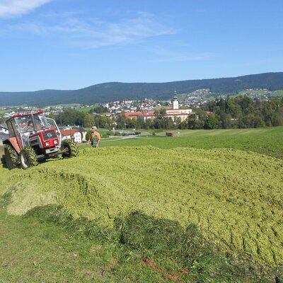 Ein Traktor auf einem Silohaufen während der landwirtschaftlichen Arbeit auf dem Bauernhof, mit einem Dorf im Hintergrund.