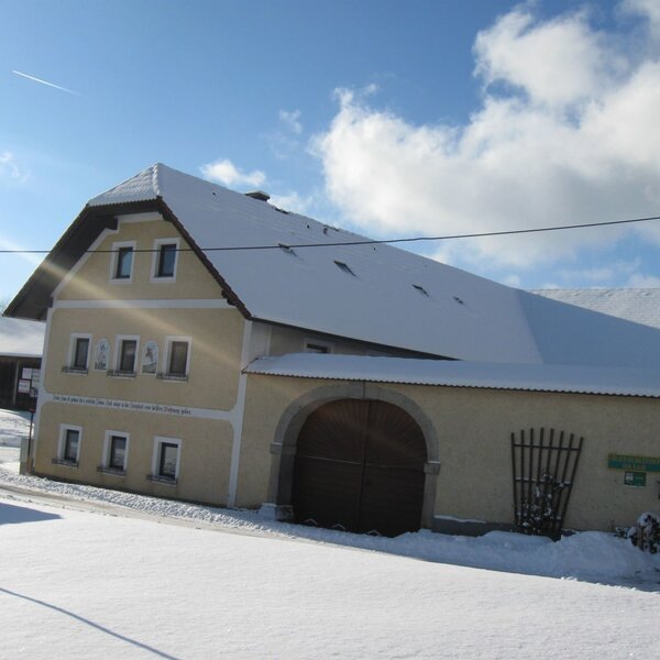 Außenansicht des Bauernhofs im Winter mit schneebedecktem Dach und gelber Fassade.