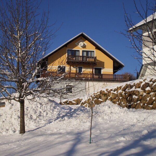 Der Bauernhof mit gelber Fassade und Balkonen, eingebettet in eine winterliche Schneelandschaft.