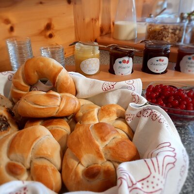 Ein Teil des Frühstücksbuffets auf dem Bauernhof mit frischen Brötchen, hausgemachten Marmeladen, Honig und roten Johannisbeeren.