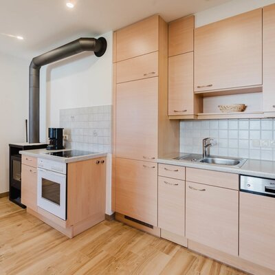 Die helle, voll ausgestattete Küche in der Wohnung des Bauernhofs mit freundlichen Holzfronten und einem urigen Kaminofen.