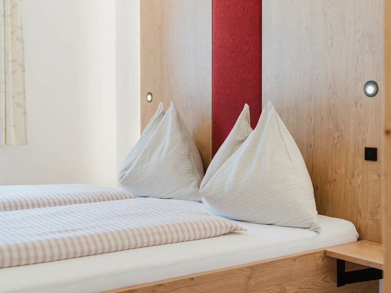 Ein gemütliches Doppelbett mit einladender, gestreifter Bettwäsche und warmem Holz-Kopfteil auf dem Bauernhof.
