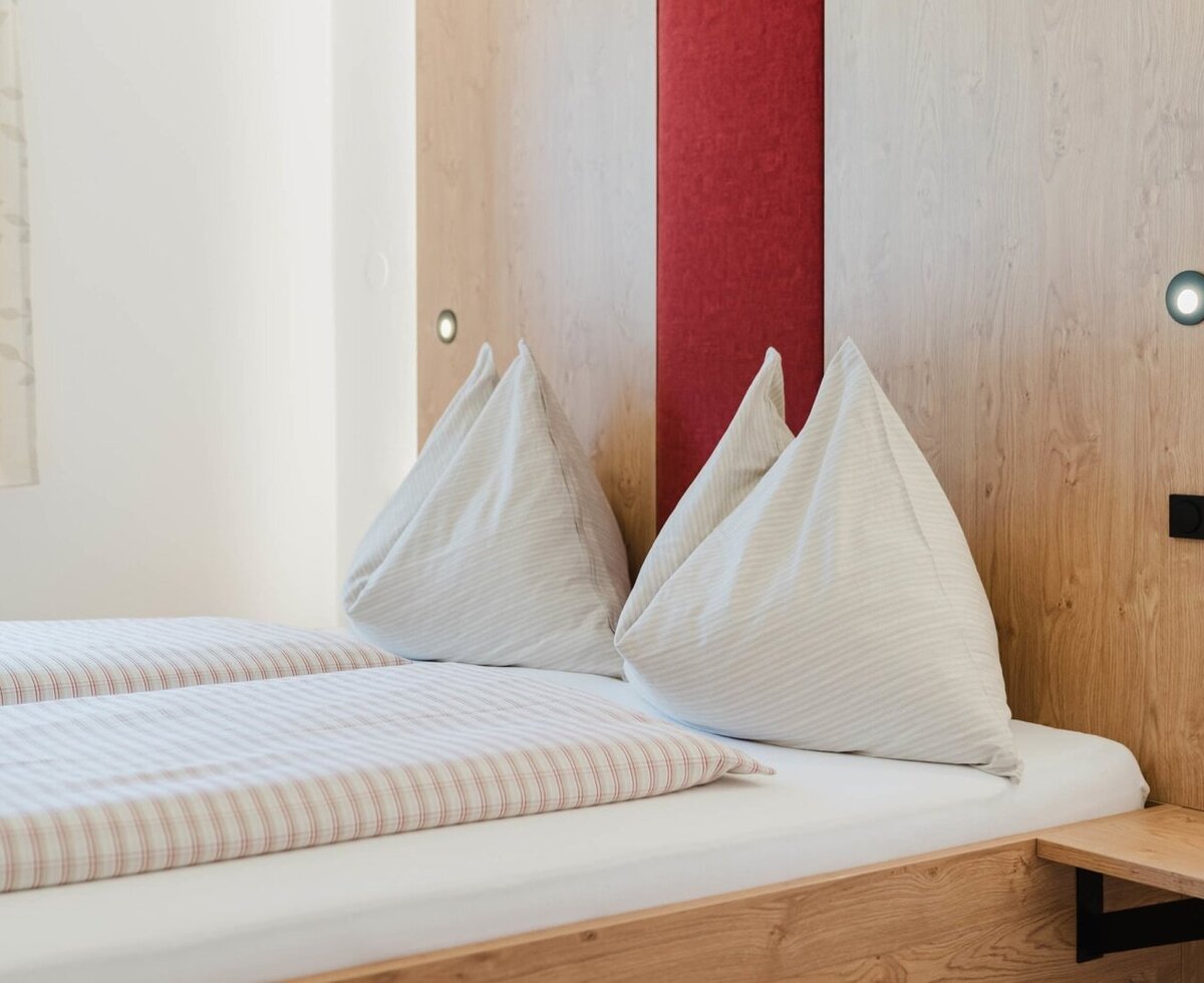 Ein gemütliches Doppelbett mit einladender, gestreifter Bettwäsche und warmem Holz-Kopfteil auf dem Bauernhof.