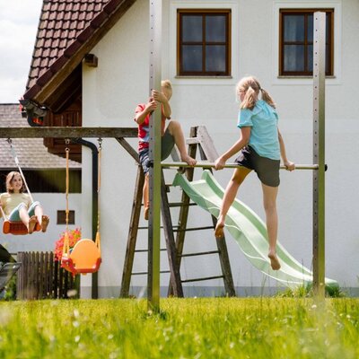 Der Spielplatz des Bauernhofs mit Schaukeln, Rutsche und Kletterbereich.