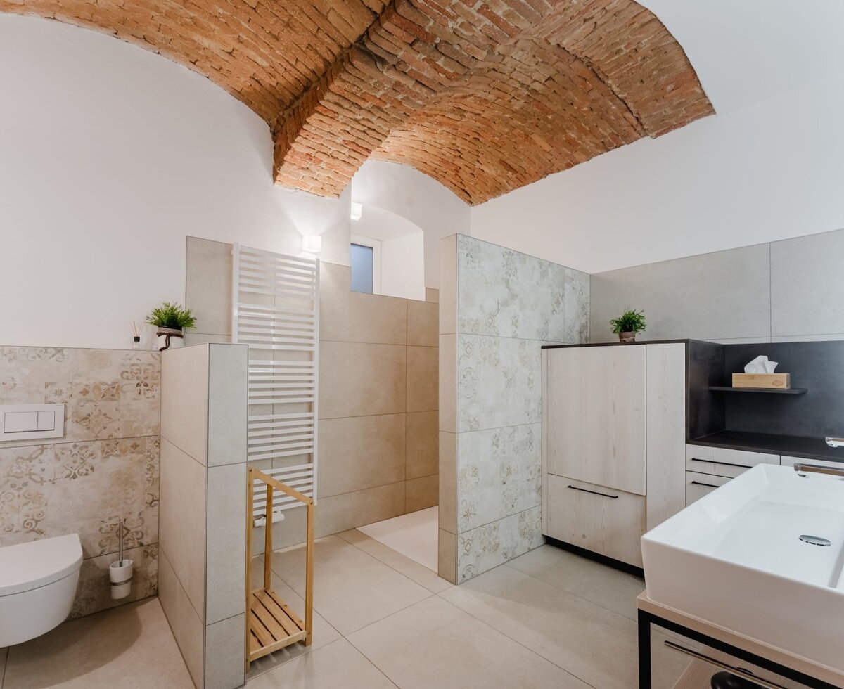 Modernes Badezimmer im Bauernhof mit großer Dusche, wandhängendem WC, Waschtisch, Handtuchheizkörper und einer Ziegelgewölbedecke.