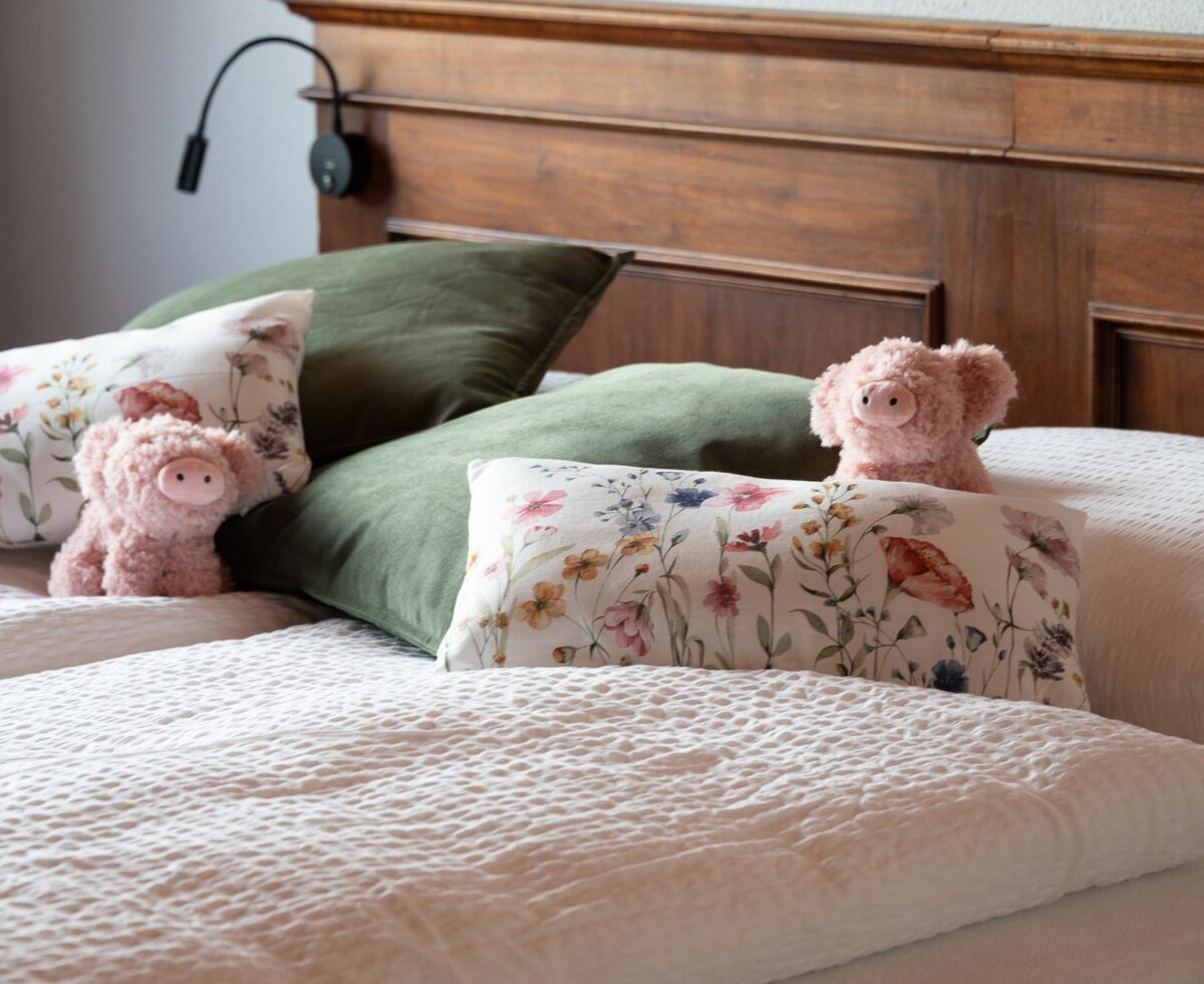 Bett im Schlafzimmer des Bauernhofs mit massivem Holzkopfteil, selbstgenähten Schafwollbetten und floralen Kissen.