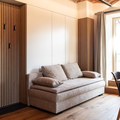 Wohnbereich im Bauernhof mit Sofa, integrierter Garderobe, Esstisch am Fenster und Holzboden.