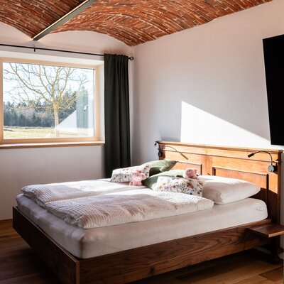 Doppelschlafzimmer im Bauernhof mit Vollholzbett, selbstgenähten Schafwollbetten, gewölbter Backsteindecke, TV und Fenster mit Ausblick.