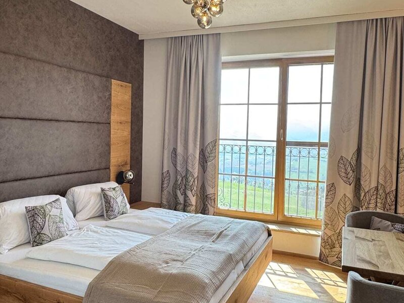 Doppelzimmer im Bauernhof mit Holzbett, gepolstertem Kopfteil, einem Tisch mit Stühlen und Blick auf die Landschaft.