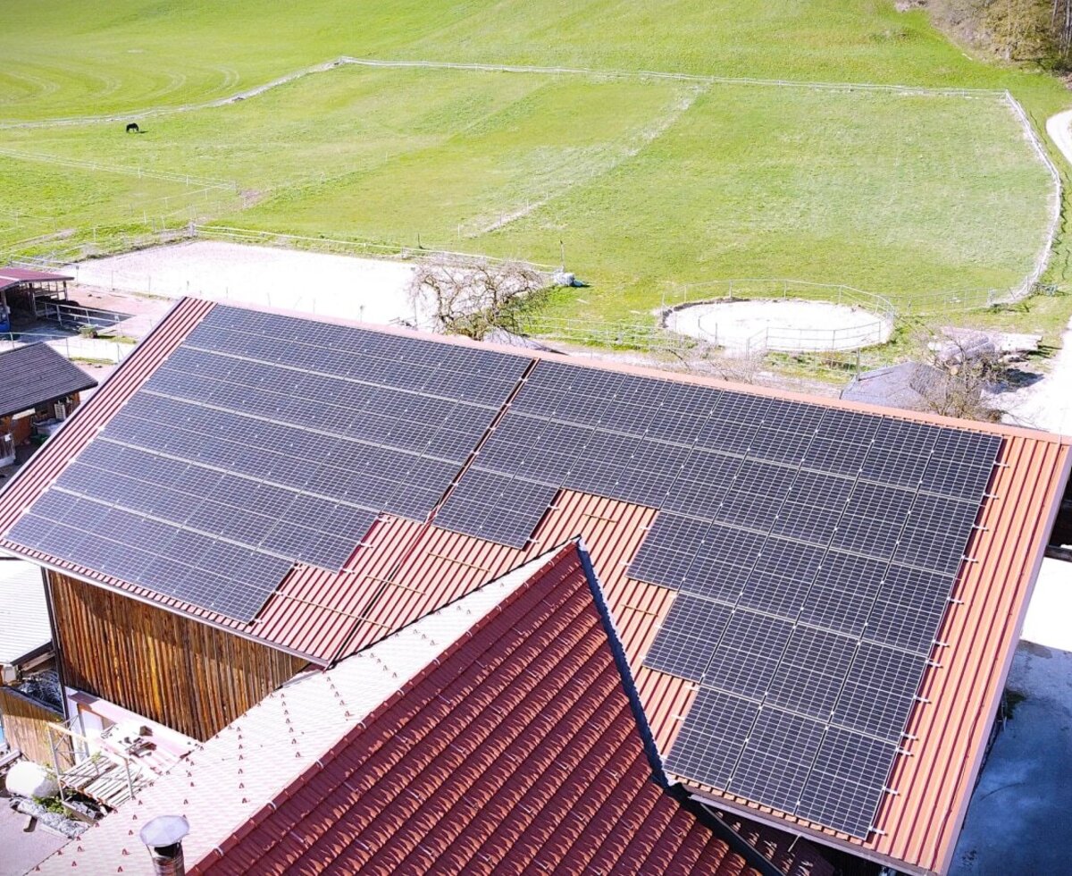 Eine Luftaufnahme des Bauernhofs mit modernen Solarmodulen auf dem Dach, umgeben von saftig grünen Wiesen.