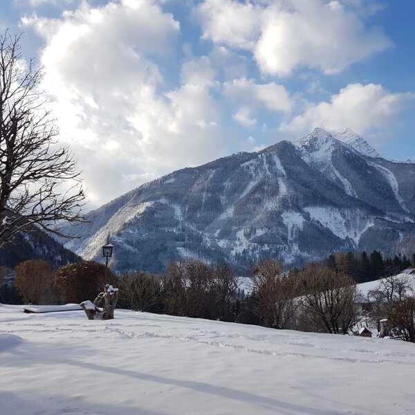 Der verschneite Gartenbereich des Bauernhofs mit sichtbarem Spielplatz und Bergen im Hintergrund.