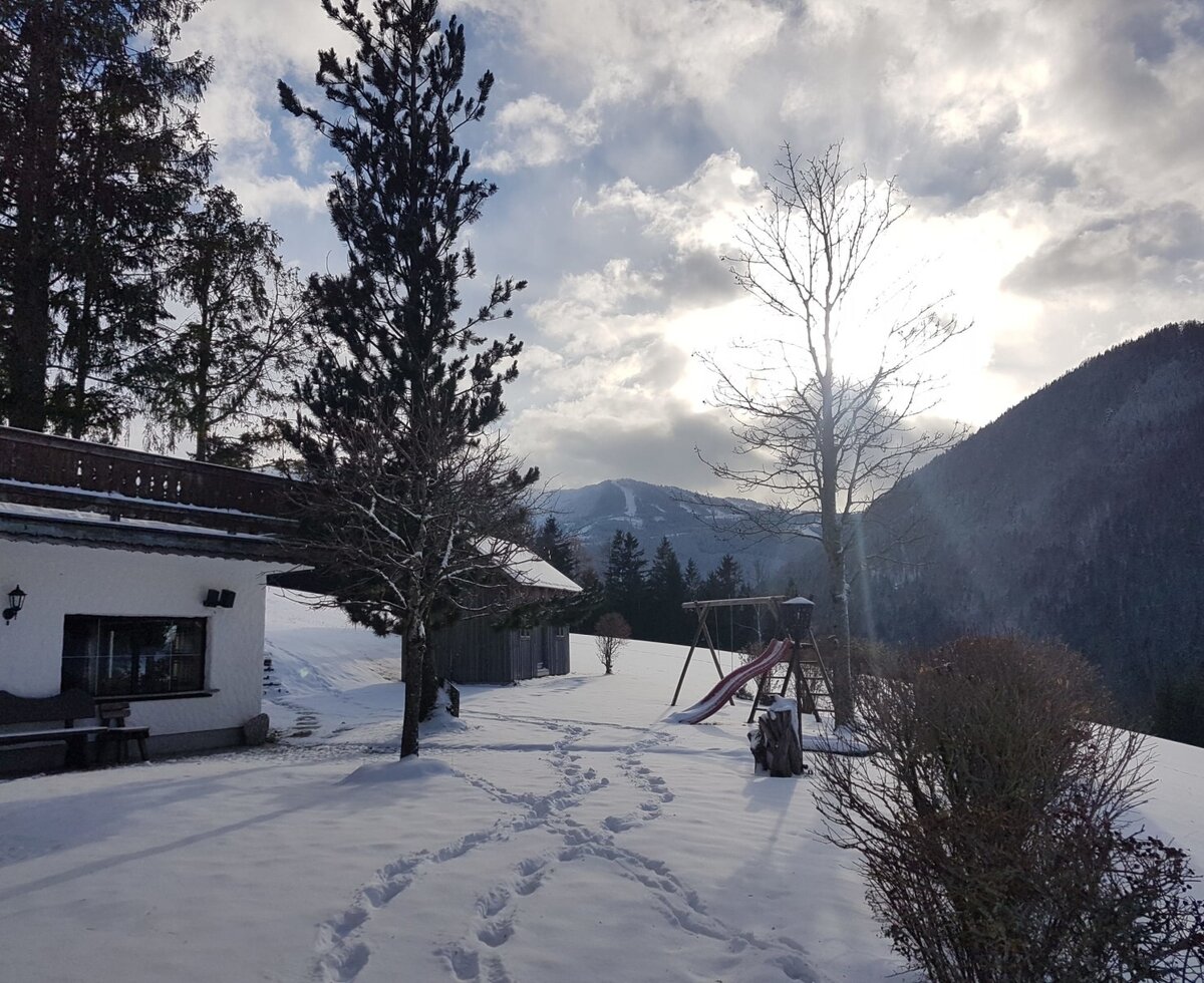 Der verschneite Garten des Bauernhofs mit einem Spielplatz und Bergblick.