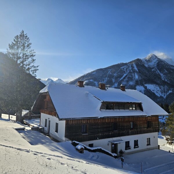 Der schneebedeckte Bauernhof mit traditioneller Holzfassade und Bergblick.