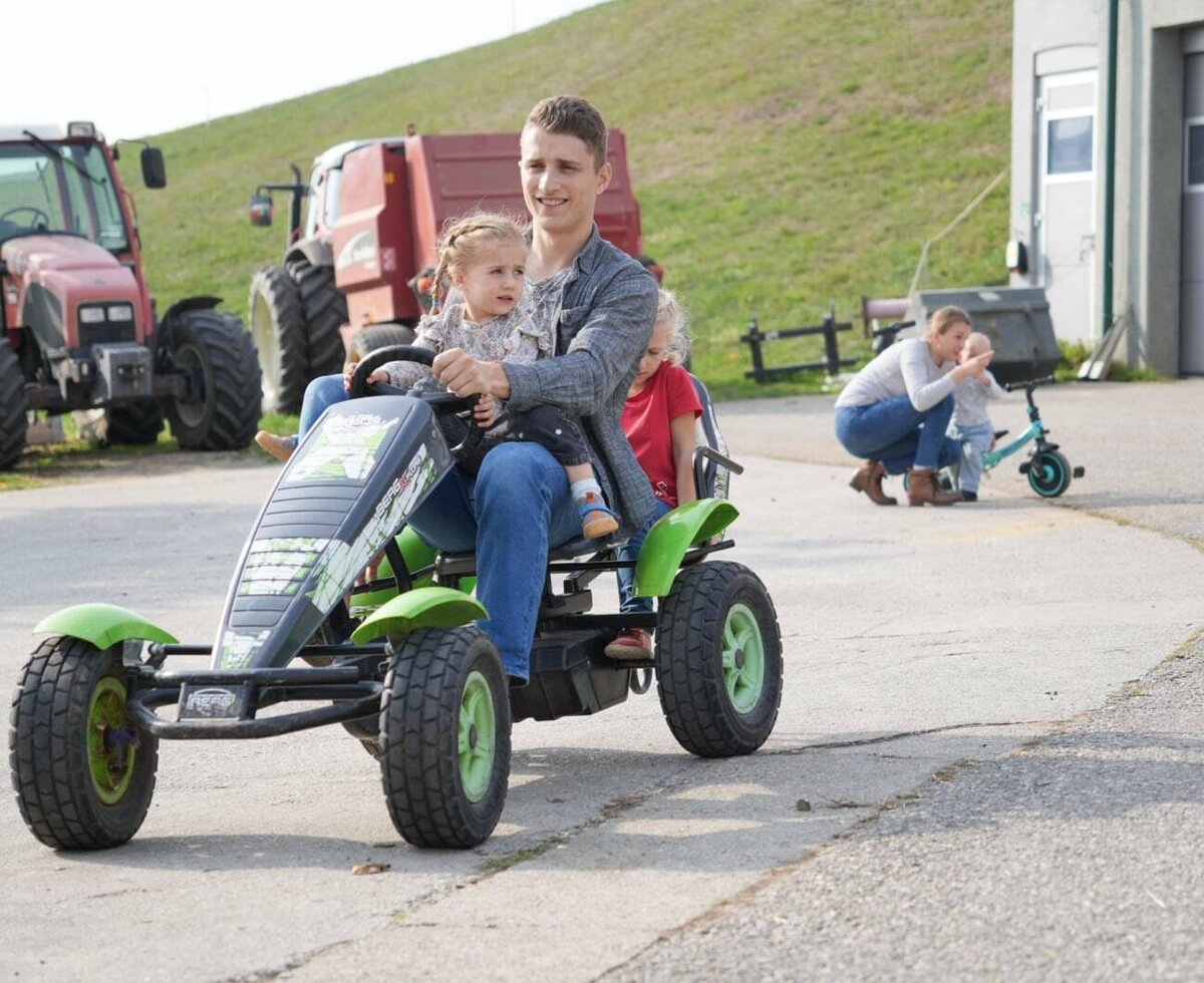 Ein einladender Bauernhof mit viel Platz zum Spielen, Tretautos für Kinder und echten Traktoren im Hintergrund.