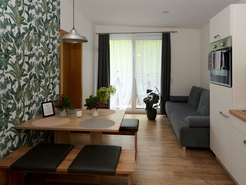 Wohnbereich einer modernen Ferienwohnung im Bauernhof mit Essplatz, Sofa, integrierter Küche und direktem Zugang zum Balkon.