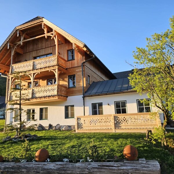 Außenansicht des Appartementsgebäudes mit traditioneller Holzfassade, Balkonen und einer Terrasse mit geschnitzten Geländern.