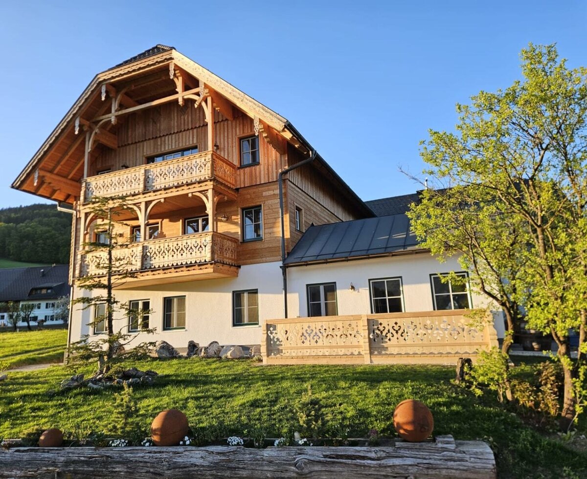 Außenansicht des Appartementsgebäudes mit traditioneller Holzfassade, Balkonen und einer Terrasse mit geschnitzten Geländern.