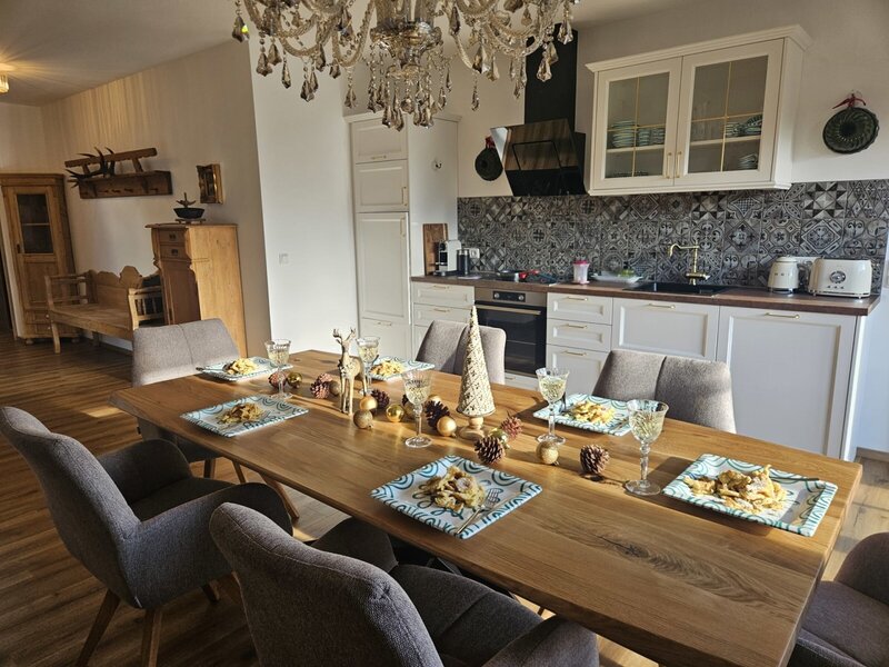 Essbereich mit großem Holztisch und Stühlen, kombiniert mit einer modernen, voll ausgestatteten Küche in einem Appartement.