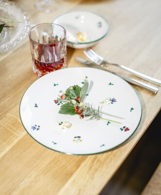 Gedeckter Tisch in den Appartements mit einem Teller, Besteck, einem Glas und einer Dekoration aus Wilderdbeeren und Kr&auml;utern.