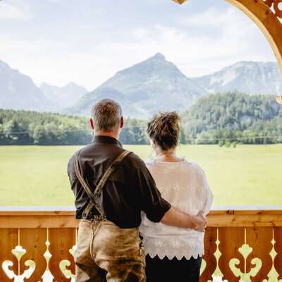Balkon eines Appartements mit traditionellem Holzgeländer und weitem Blick auf das Bergpanorama und grüne Wiesen.