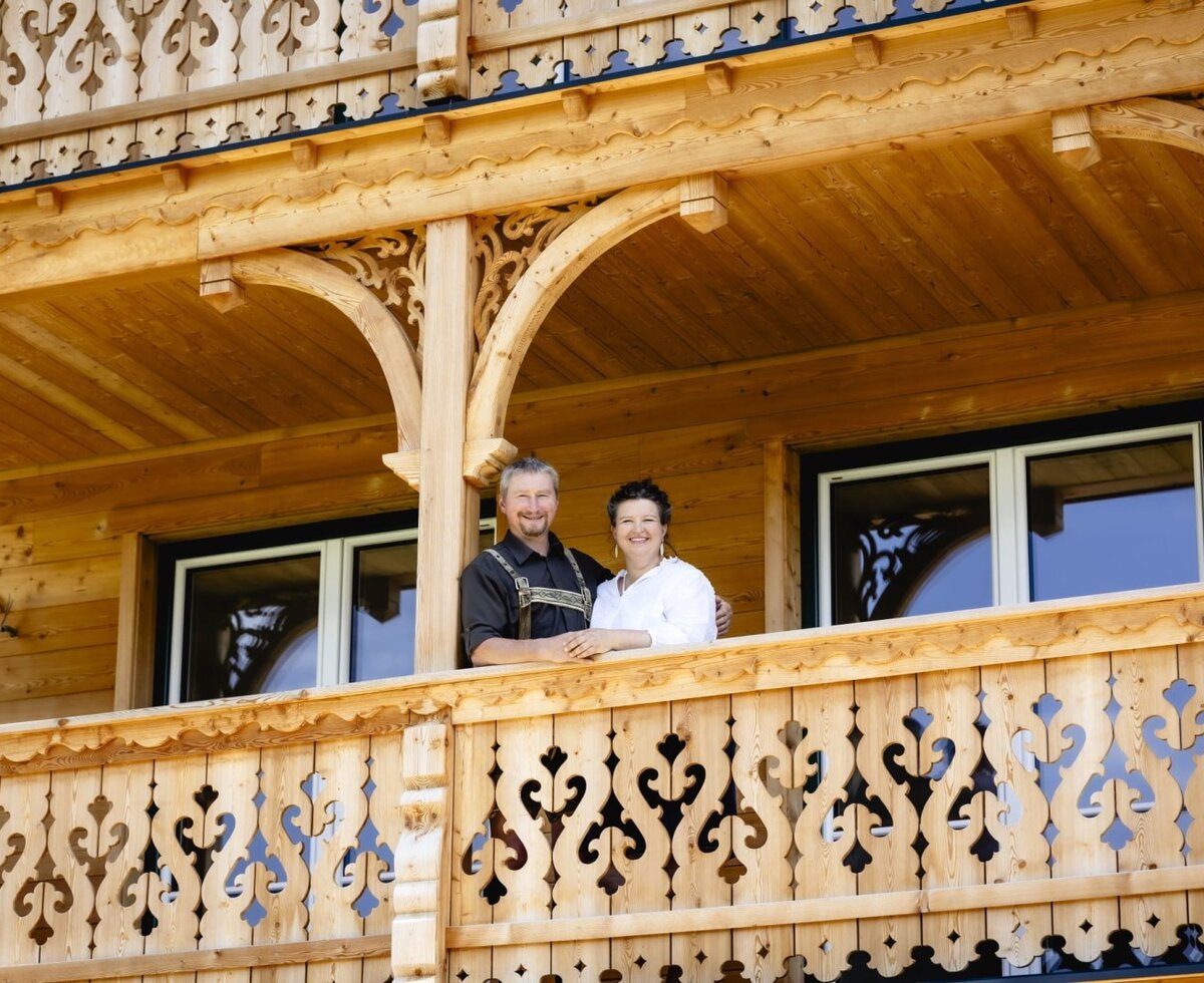 Die Gastgeber der Appartements stehen auf dem Balkon mit geschnitzten Holzgeländern.