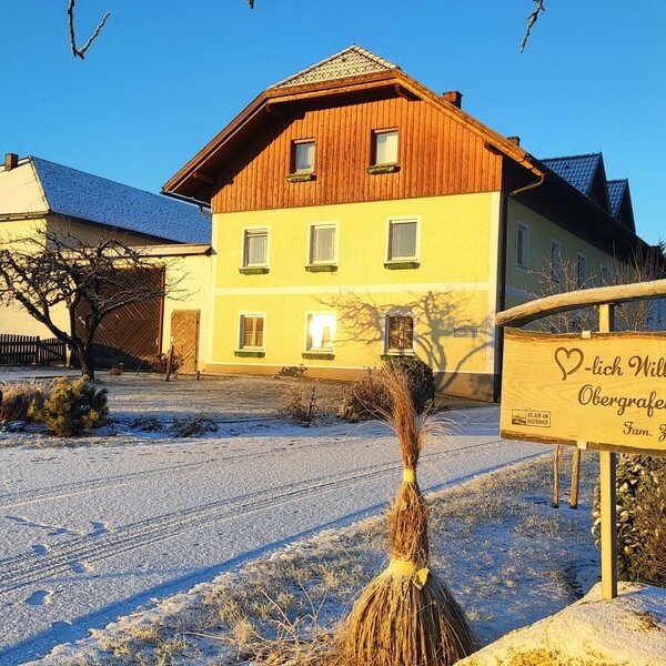Außenansicht des Bauernhofs im Winter mit verschneitem Grundstück und einem Willkommensschild am Eingang.