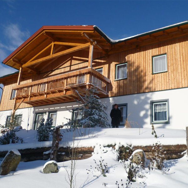 Außenansicht des Bauernhofs im Winter mit schneebedecktem Grundstück und einem Holzbalkon.