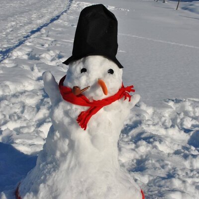 Ein Schneemann mit Zylinder, rotem Schal, Karottennase und Pfeife im verschneiten Gelände des Bauernhofs.