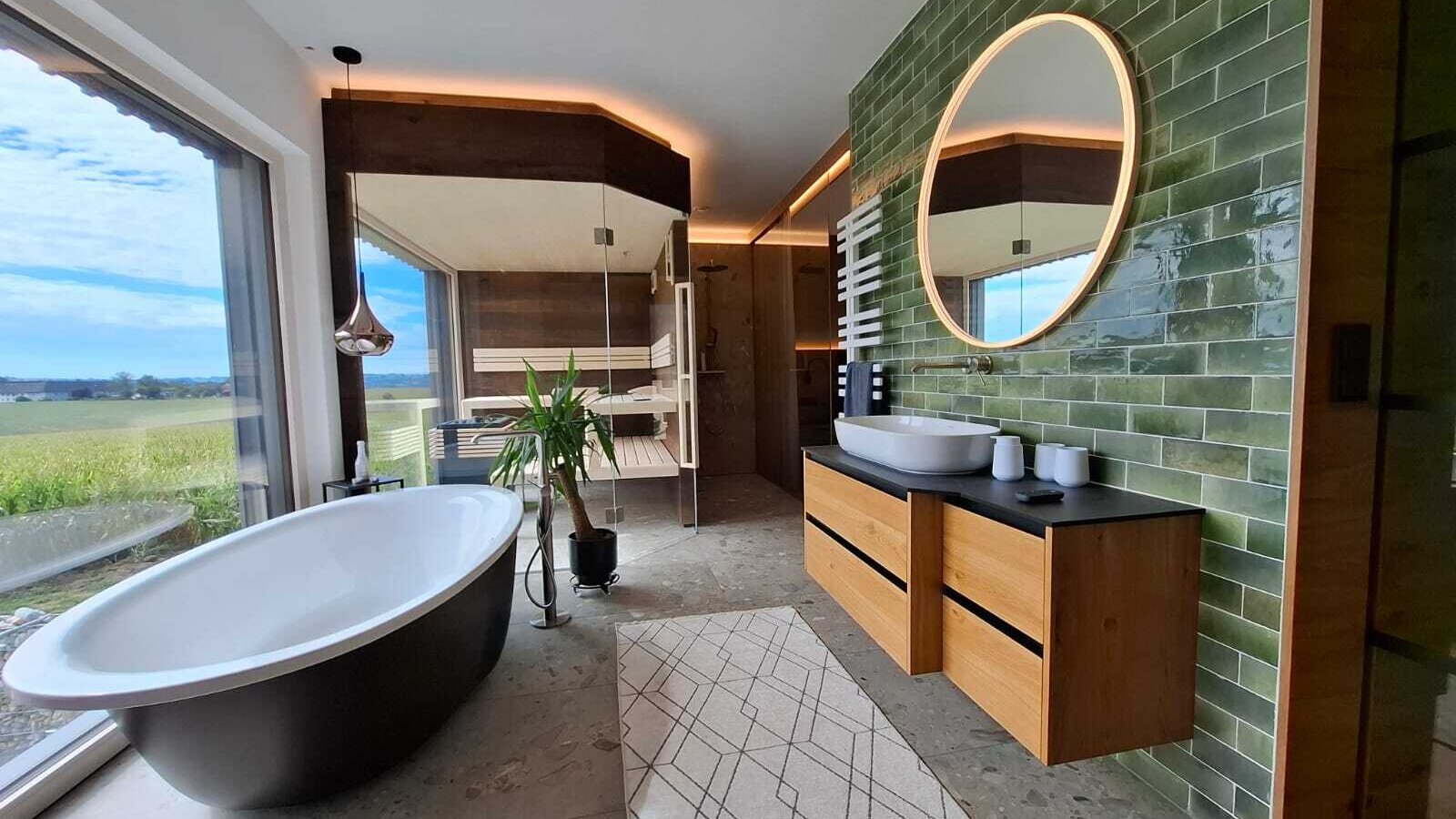 Das luxuriöse Badezimmer des Ferienhauses mit freistehender Badewanne, einer Sauna und Panoramablick ins Grüne.