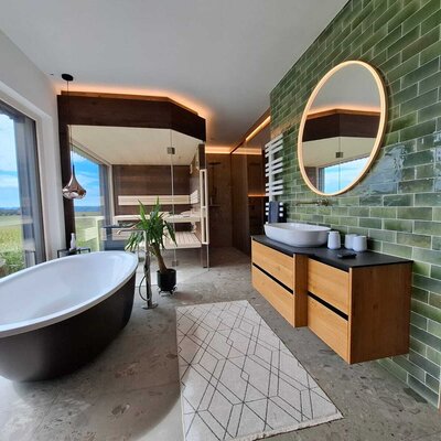 Das luxuriöse Badezimmer des Ferienhauses mit freistehender Badewanne, einer Sauna und Panoramablick ins Grüne.