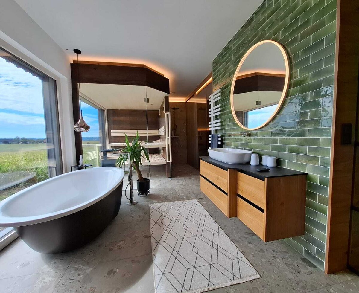 Das luxuriöse Badezimmer des Ferienhauses mit freistehender Badewanne, einer Sauna und Panoramablick ins Grüne.