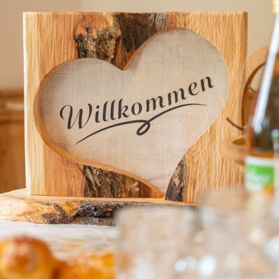 Ein herzliches, aus Holz gestaltetes Willkommensschild empfängt die Gäste im Bauernhof.