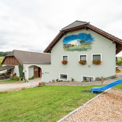 Der einladende Bauernhof mit einer gepflegten grünen Wiese, einem kleinen Kinderspielplatz und einer kunstvollen Wandmalerei.