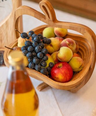 Ein einladender, hölzerner Obstkorb mit frischen Äpfeln, Pfirsichen und Weintrauben auf dem Bauernhof.