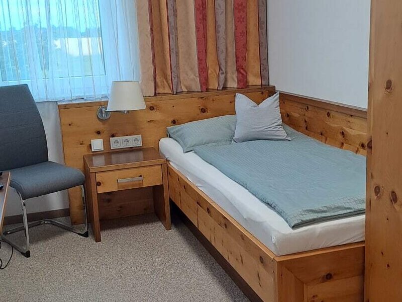Ein gemütliches Zimmer mit einem rustikalen Holz-Einzelbett, hellem Fenster und einladenden Holzmöbeln.