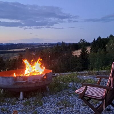 Eine einladende Feuerstelle mit gemütlichen Sesseln und weitem Panoramablick über die Hügellandschaft bei der Riederegger-Alm.