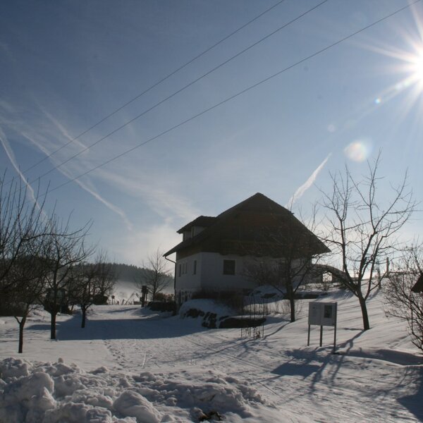 Der Bauernhof liegt in einer sonnigen Winterlandschaft mit verschneiten Wegen und Informationstafeln.