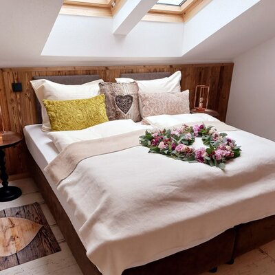 Doppelzimmer im Bauernhof mit Holzwandvertäfelung, Dachfenstern, Nachttischen und einer herzförmigen Fußmatte.