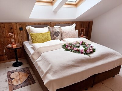 Doppelzimmer im Bauernhof mit Holzwandvertäfelung, Dachfenstern, Nachttischen und einer herzförmigen Fußmatte.