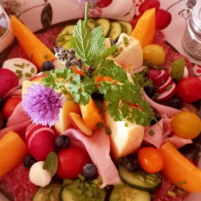 Eine Frühstücksplatte mit Käse, Wurst, frischem Gemüse, Obst und Kräutern, ergänzt durch Eier und weitere Bauernhofprodukte.