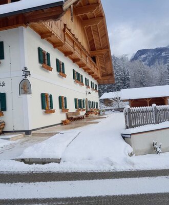 Außenansicht des Bauernhofs im Winter, mit Schnee bedeckt, traditionellen Holzbalkonen und grünen Fensterläden.