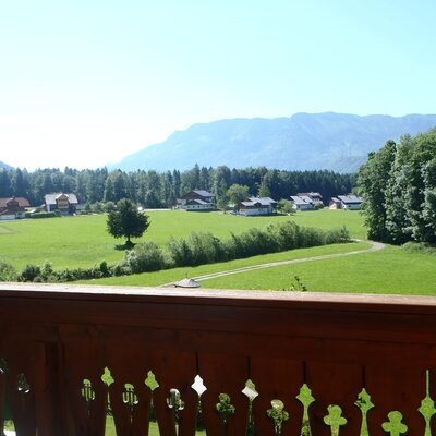 Aussicht vom Balkon des Bauernhofs auf grüne Wiesen, vereinzelte Häuser, Wälder und Berge im Hintergrund.