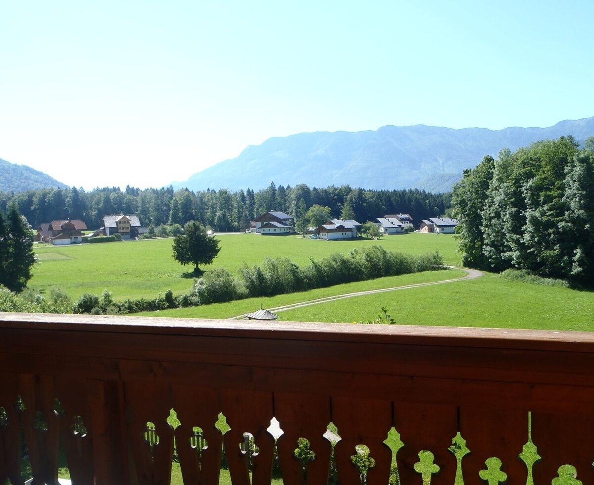 Aussicht vom Balkon des Bauernhofs auf grüne Wiesen, vereinzelte Häuser, Wälder und Berge im Hintergrund.
