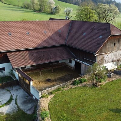 Das Hauptgebäude des Biohofs Grubbauer mit rotem Ziegeldach und angrenzendem Tierbereich.
