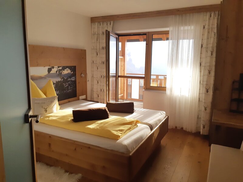 Doppelzimmer im Bauernhof mit Holzbett, einer Berglandschaft am Kopfende und Balkonzugang.